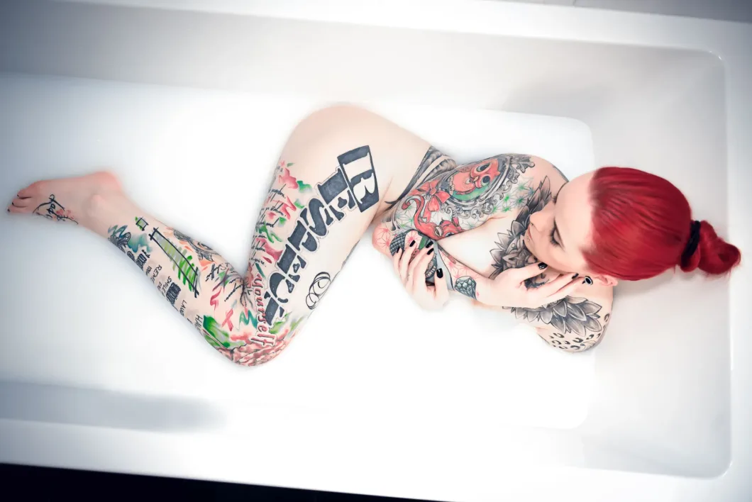 Frau mit roten Haaren und Tattoos liegt in einer Badewanne voller Wasser.