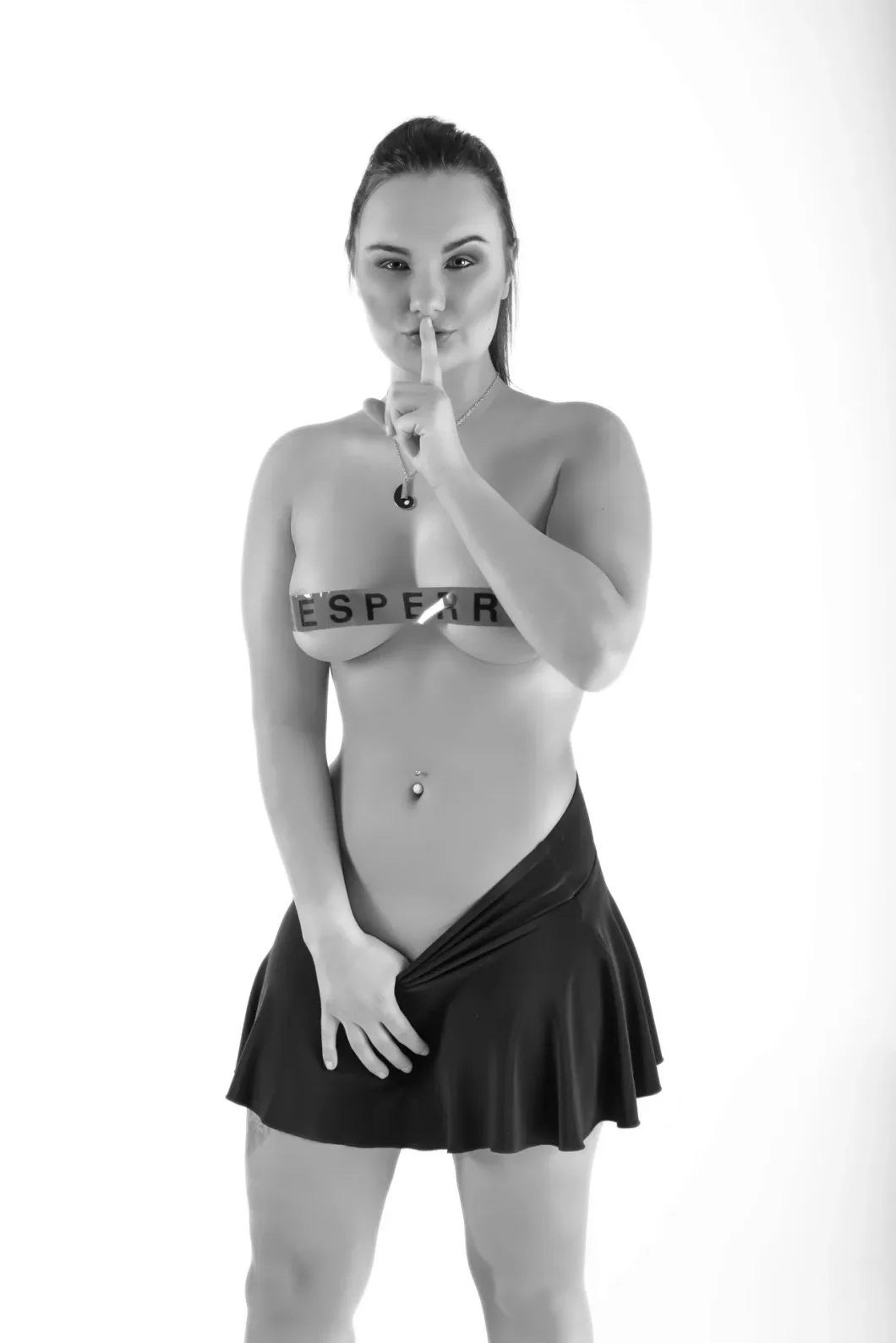 Frau in Unterwäsche hält Finger an den Mund, trägt einen Rock, schwarz-weiß Fotografie.