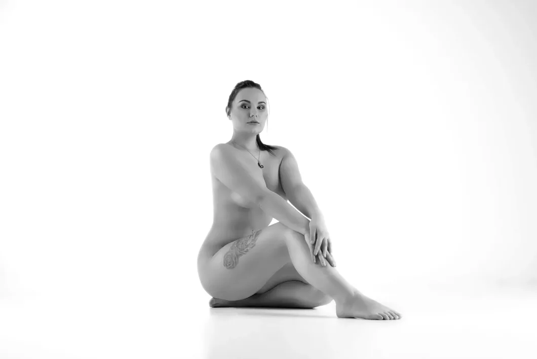 Liegende Frau in Schwarz-Weiß, künstlerische Pose vor weißem Hintergrund.