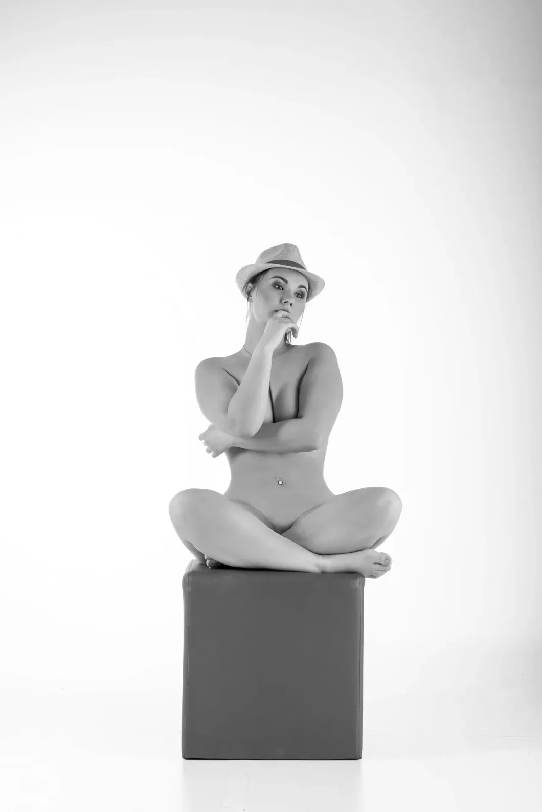 Sitzende Person mit Hut, denkt nach, monochrom aufgenommen, minimalistische Studio-Umgebung.