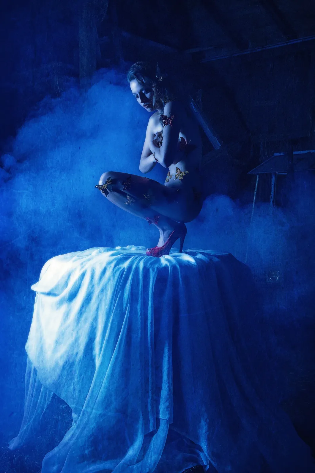 Frau auf Tisch in blauem Licht, Schmetterlinge auf der Haut, rote High Heels, umgeben von Nebel.