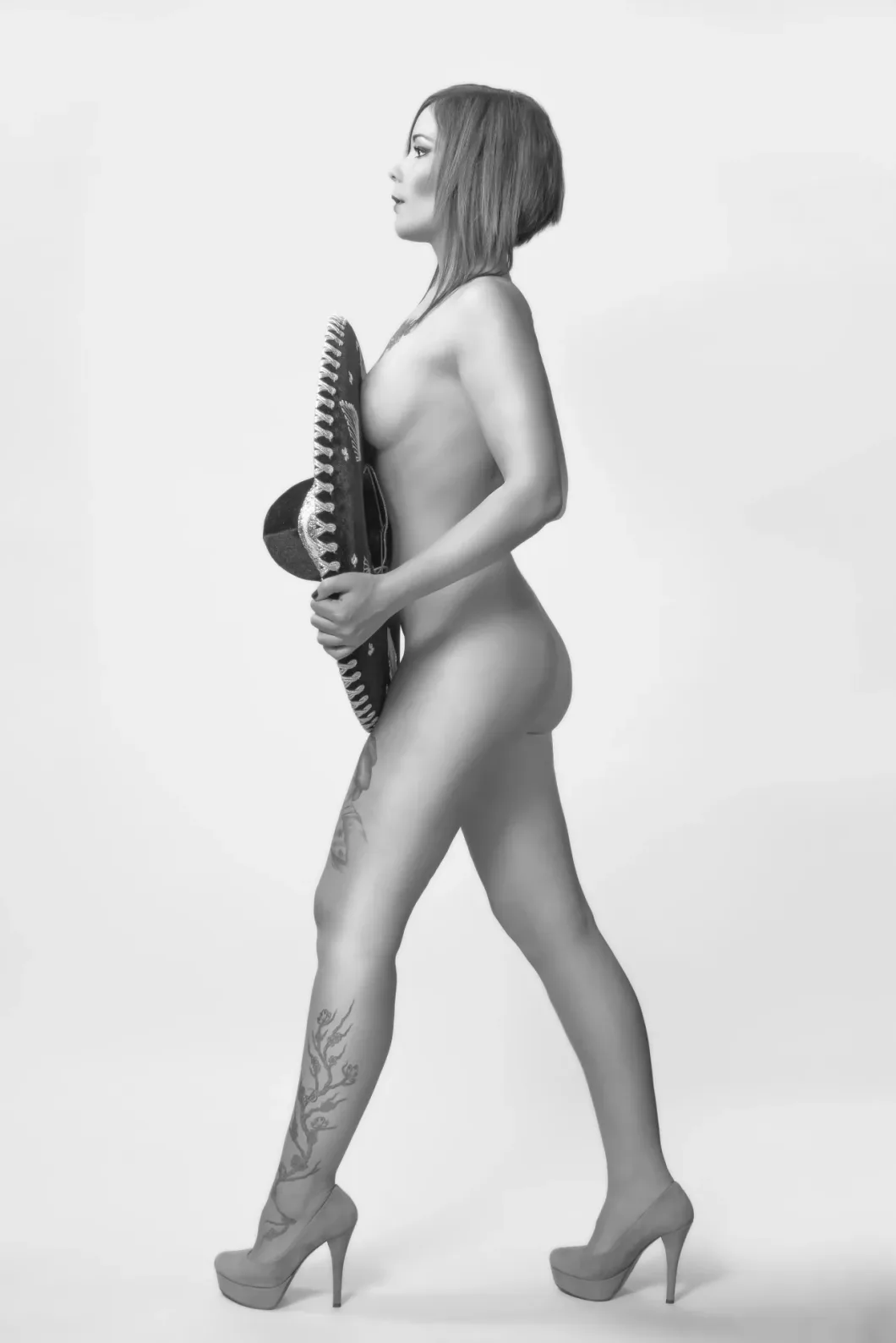 Frau mit Sombrero und High Heels, ganzseitig tätowiert, schwarz-weiß, seitliche Ansicht.