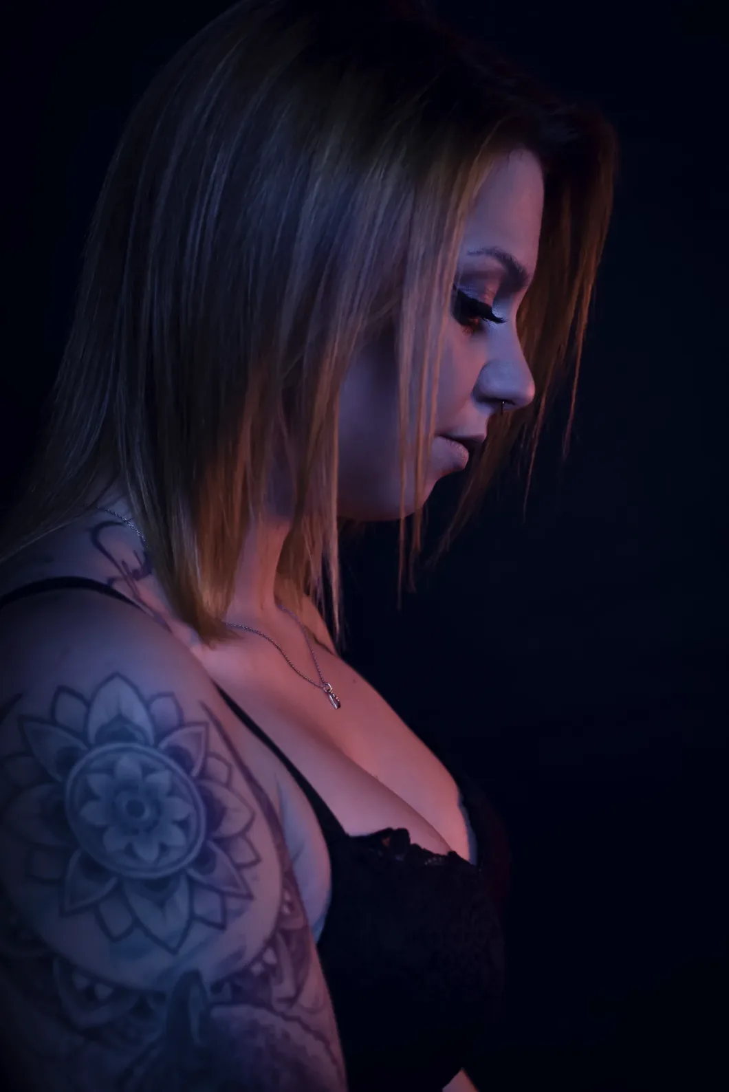Frau im Profil mit Blumen-Tattoo auf dem Arm, dunkler Hintergrund.