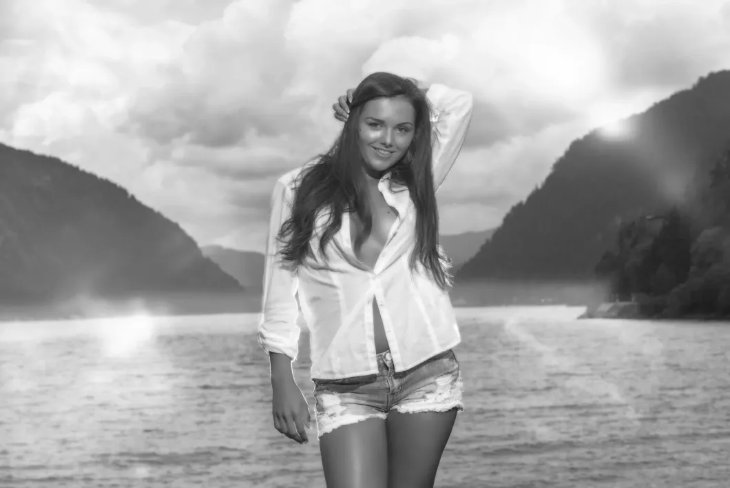 Frau in weißem Hemd und Shorts vor Bergsee-Landschaft, Schwarz-Weiß-Fotografie.