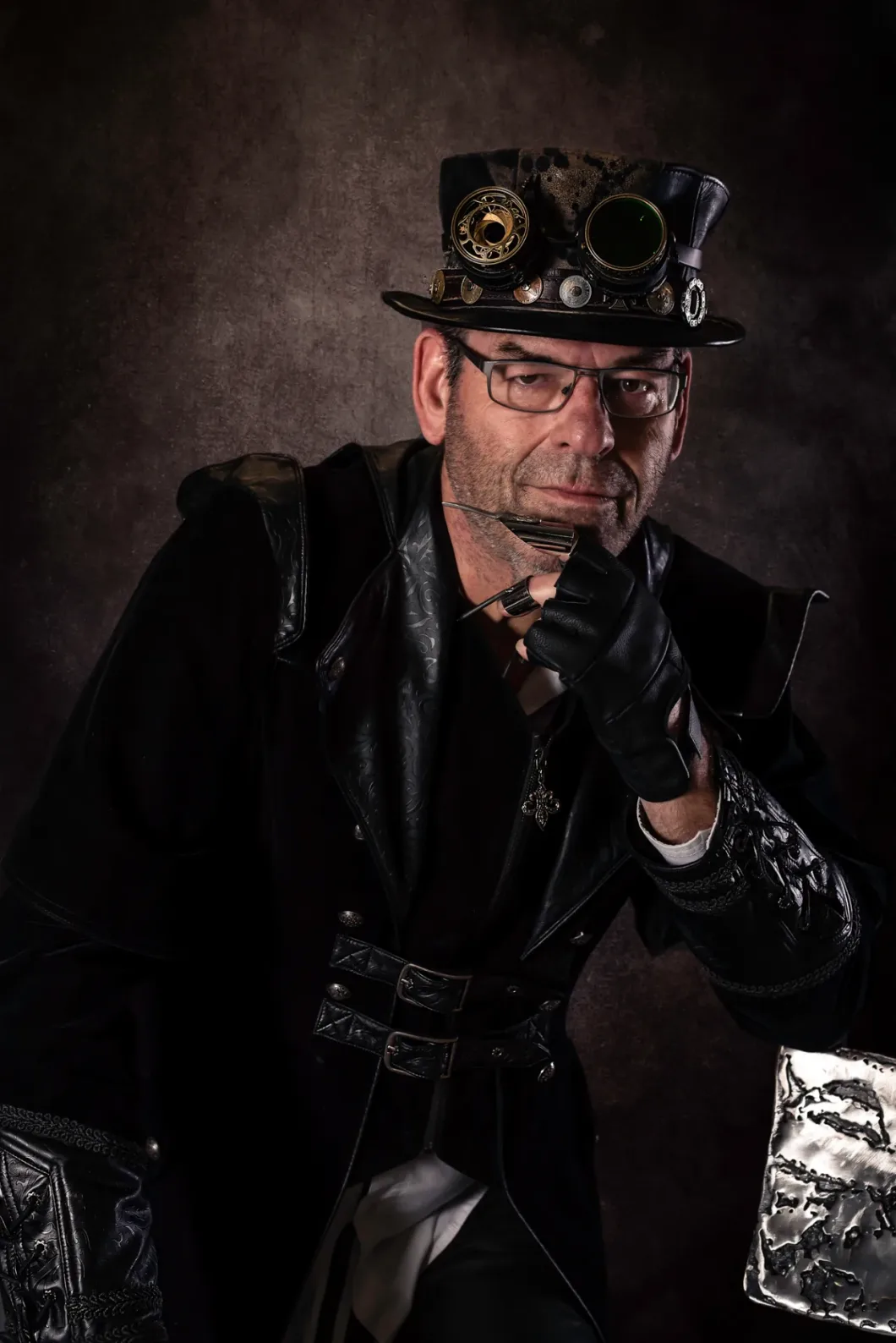 Mann im Steampunk-Outfit mit Zylinder, dekoriert mit Zahnrädern und Brille, posiert nachdenklich.