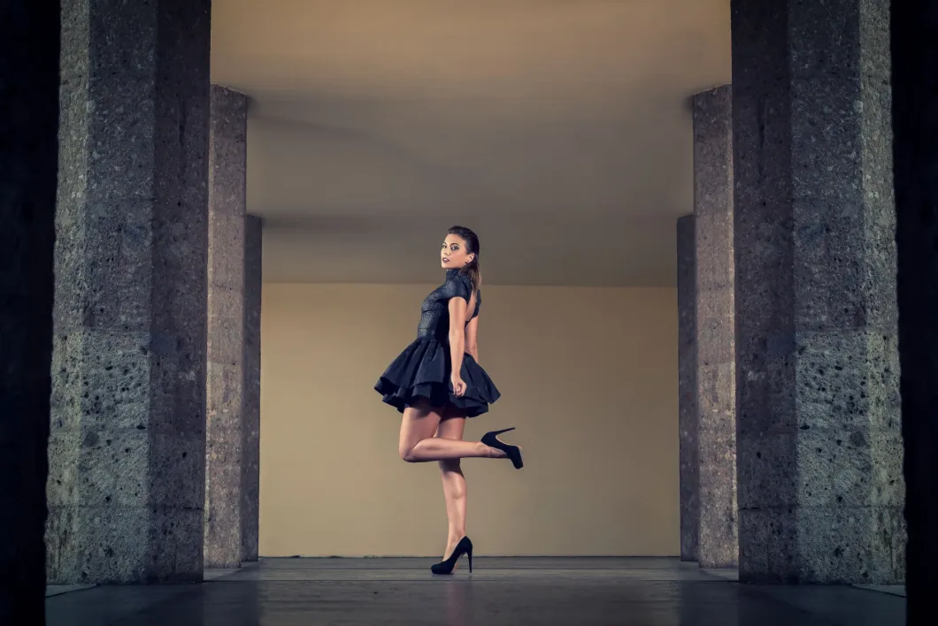 Frau im Kleid posiert elegant auf einem Bein in moderner Architekturkulisse.