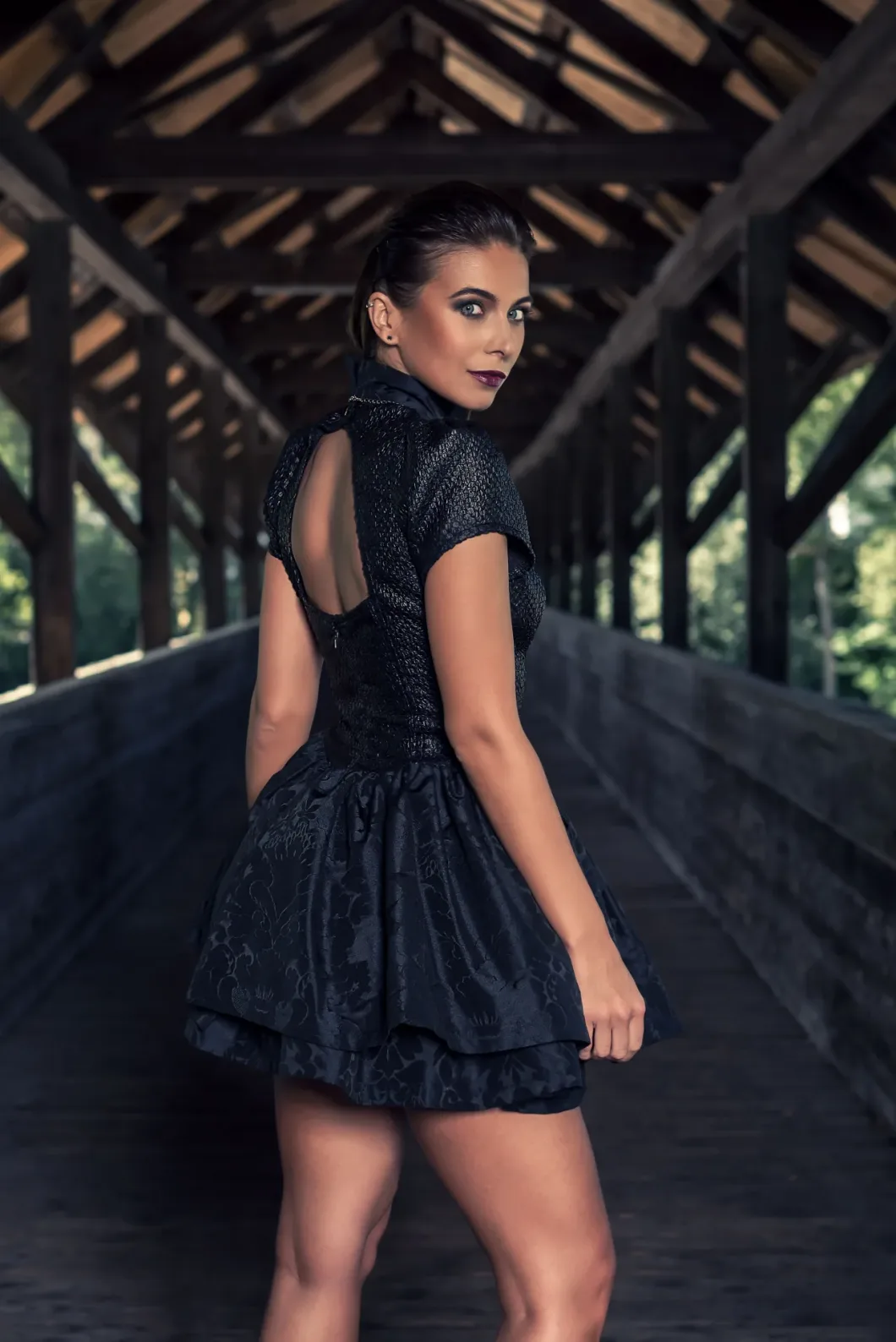 Frau in elegantem schwarzen Kleid steht auf einer überdachten Brücke.