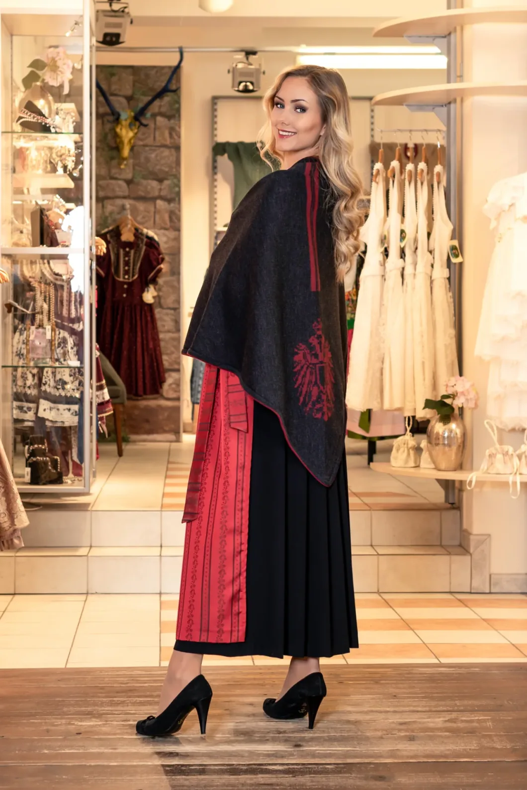Frau in Tracht mit Umhang und hochhackigen Schuhen in einem Trachtenladen.