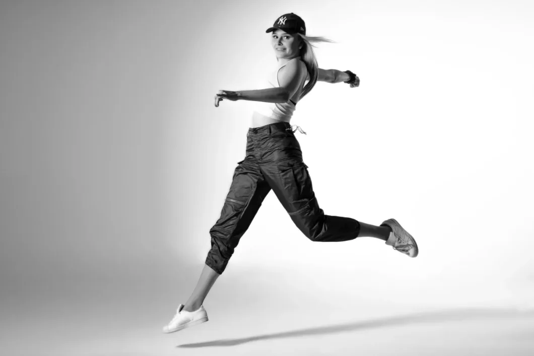 Frau mit Basecap springt dynamisch in Sportkleidung vor hellem Hintergrund.