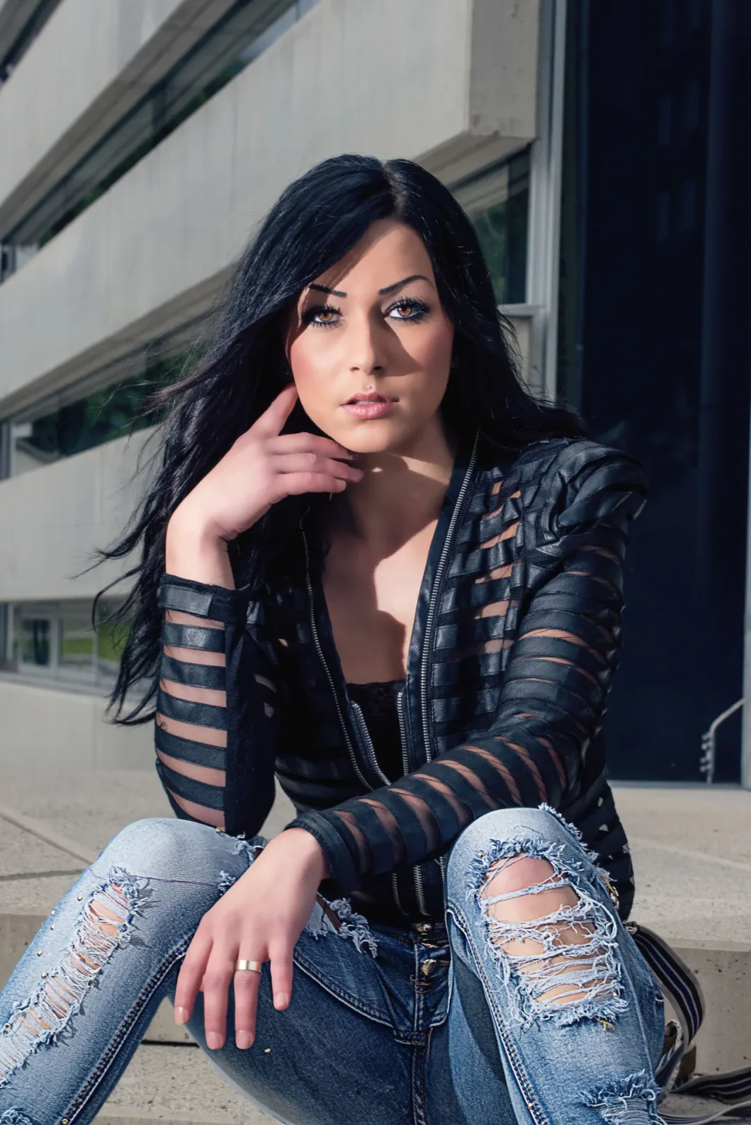 Frau in zerrissener Jeans und schwarzer Jacke vor Gebäude, nachdenklicher Blick