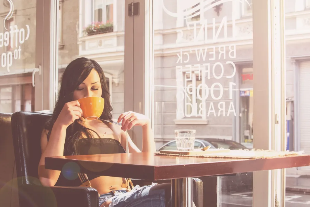 Junge Frau genießt Kaffee in modernem Café mit großen Fenstern und entspannter Atmosphäre.