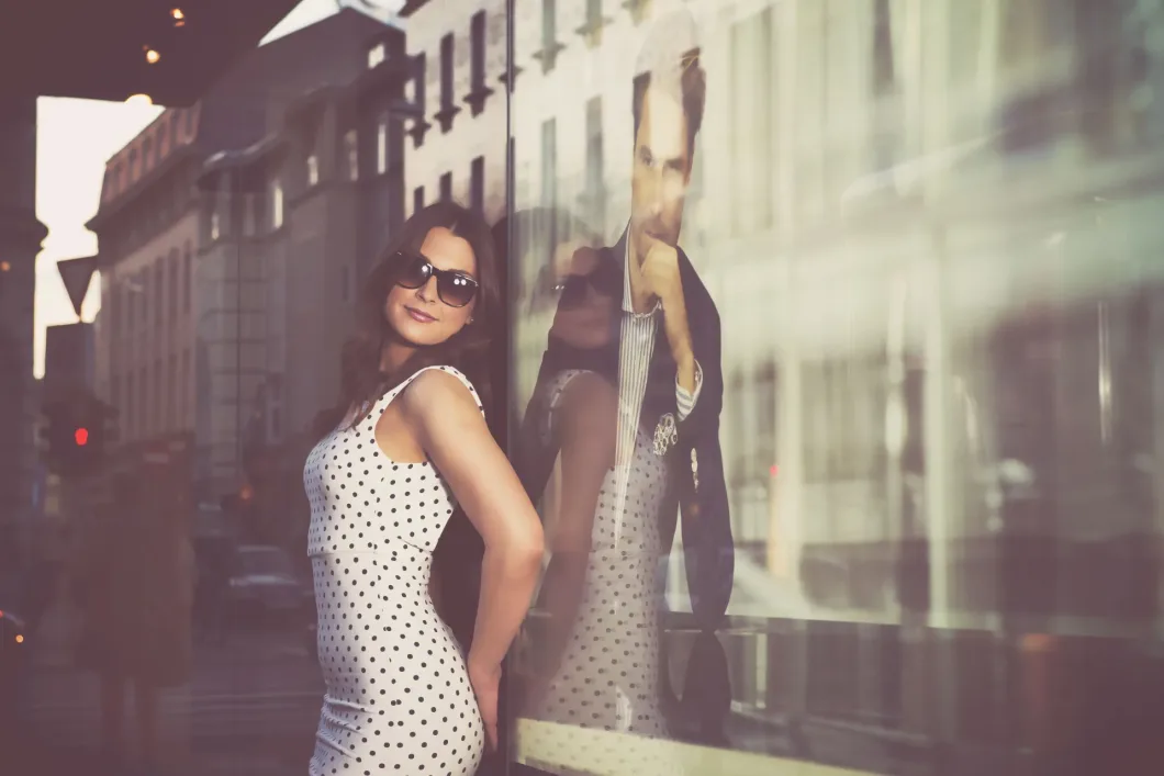Frau in gepunktetem Kleid vor spiegelndem Schaufenster mit Werbefoto.