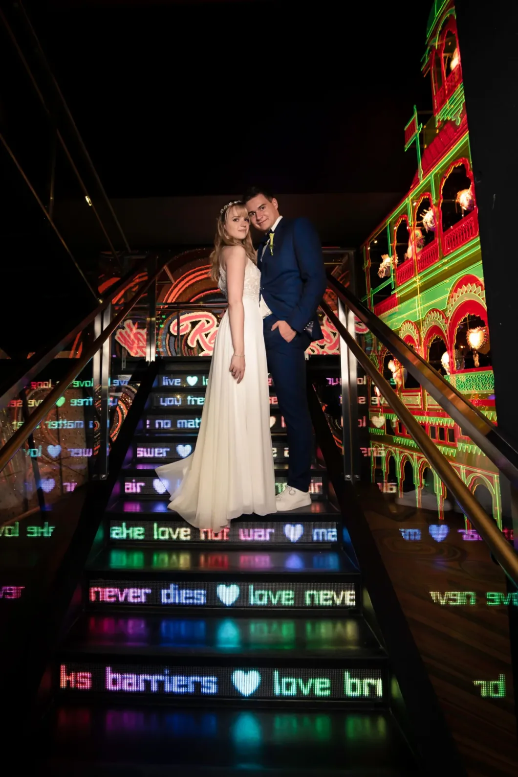 Paar auf beleuchteten Treppen mit Schrift, bunte Lichter im Hintergrund. Eleganz und Moderne.