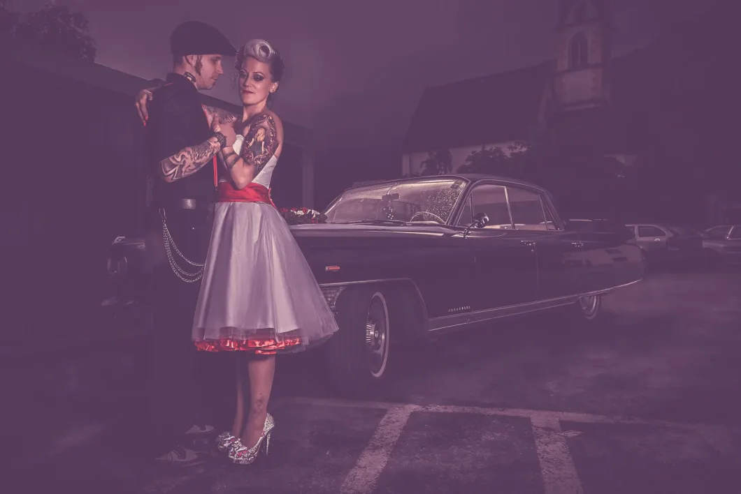 Tanzendes Paar im Vintage-Look vor klassischem Auto bei Nacht.