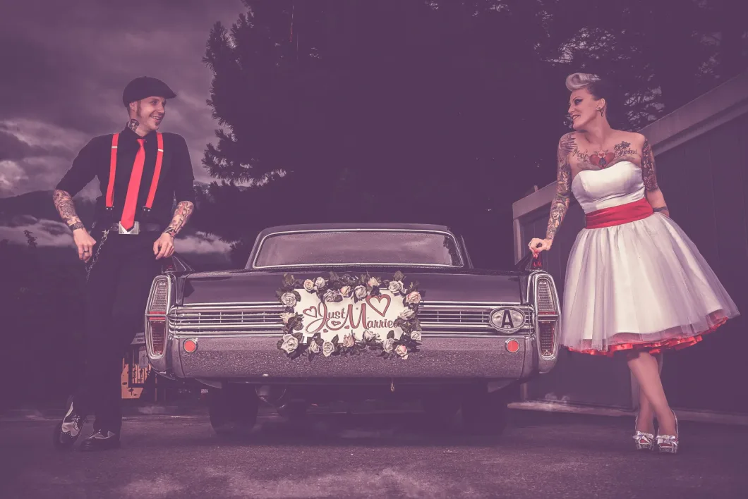 Brautpaar im Vintage-Stil vor "Just Married"-Oldtimer mit Blumen.