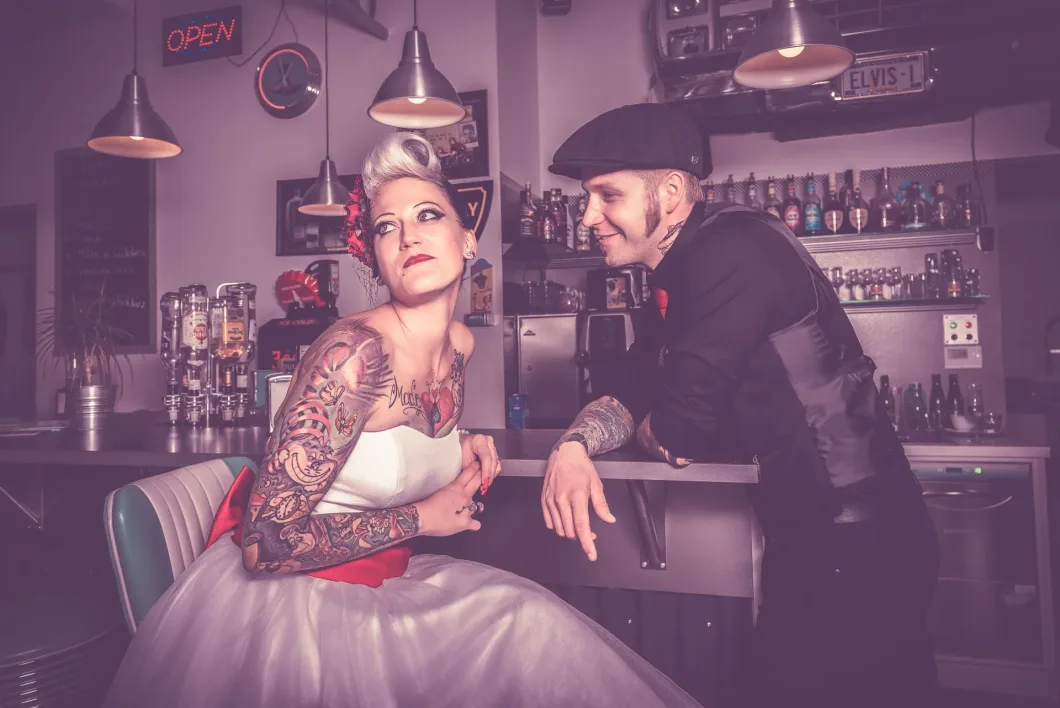 Paar im Retro-Diner mit Tattoos, Frau im Brautkleid, Mann im klassischen Look.