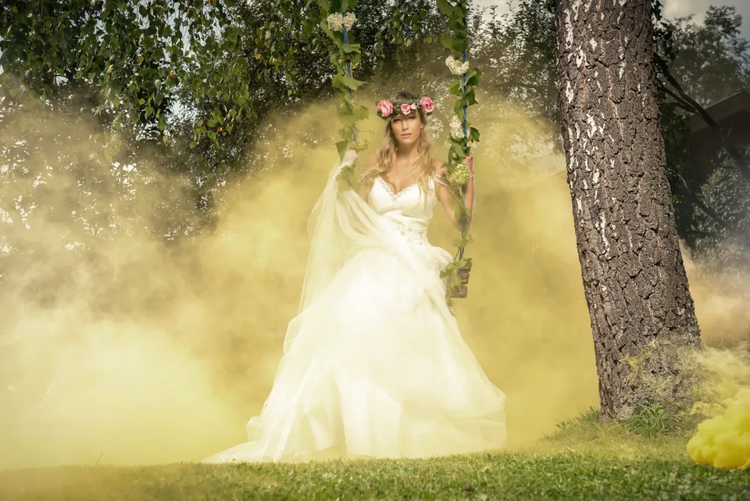 Braut auf Schaukel im Wald mit gelbem Rauch und Blumenkranz.
