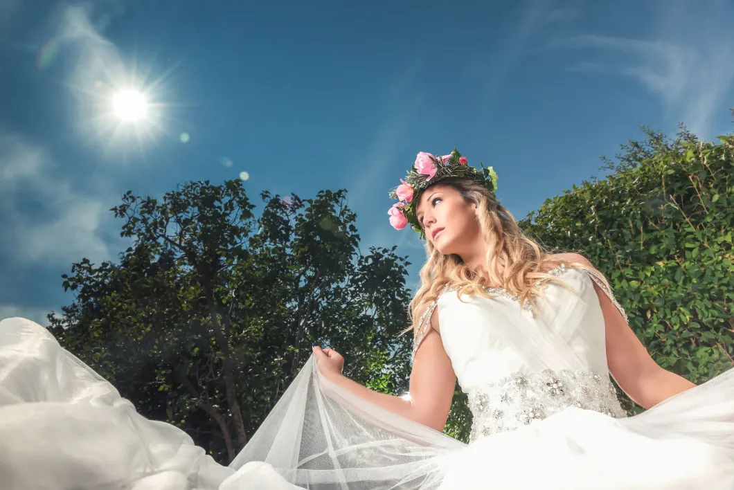 Braut mit Blumenkrone im Sonnenschein, Himmel und Büsche im Hintergrund.