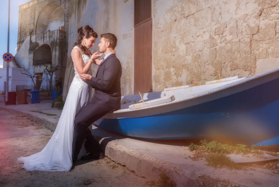 Hochzeitspaar posiert romantisch neben einem blauen Boot vor einer alten Steinmauer.