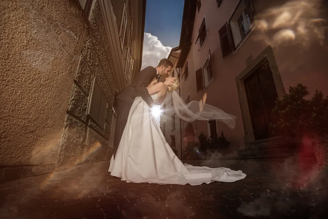 Brautpaar küsst sich in Altstadtgasse, Brautkleid reflektiert Licht.