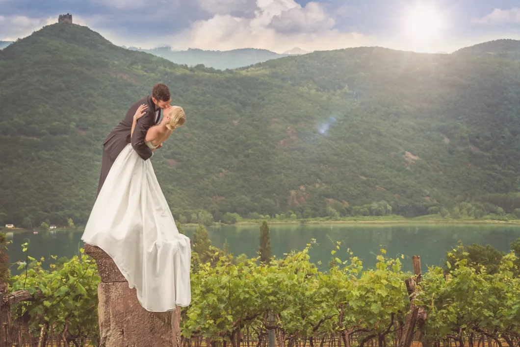 Brautpaar-Kuss auf Baumstamm vor Bergkulisse und Weinbergen im Sonnenschein.