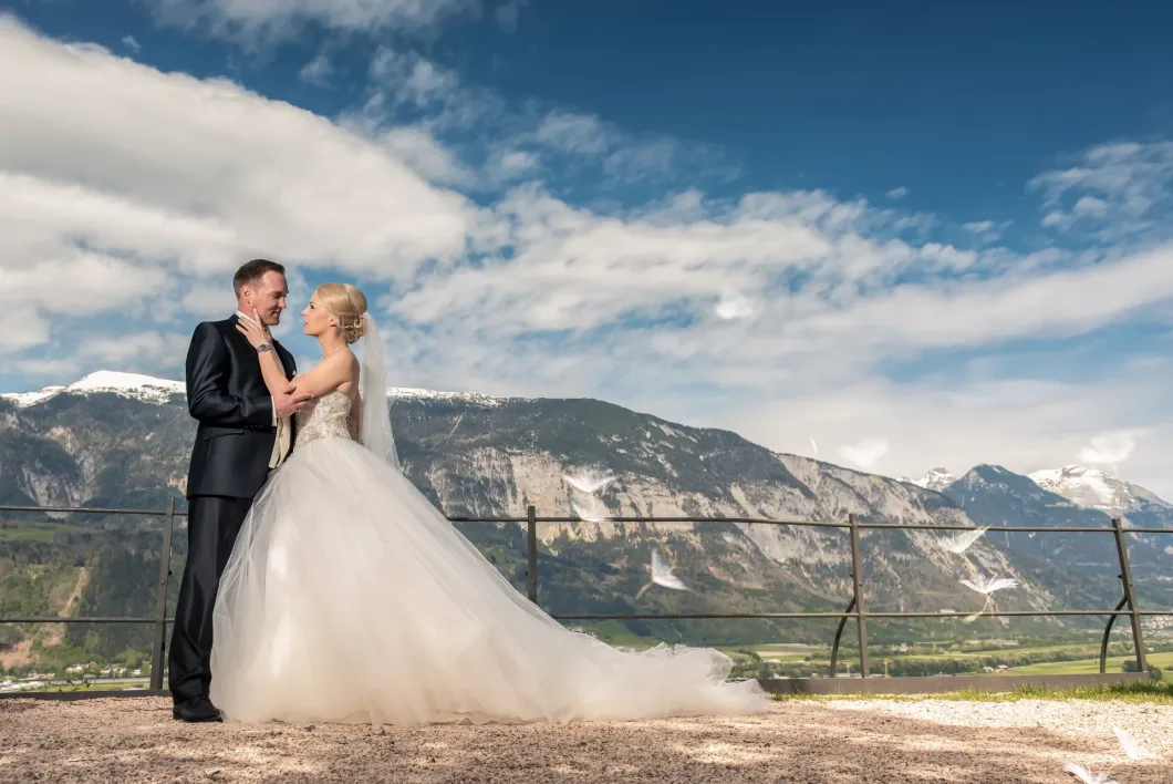 Brautpaar vor Berglandschaft in eleganter Pose bei klarem Himmel.