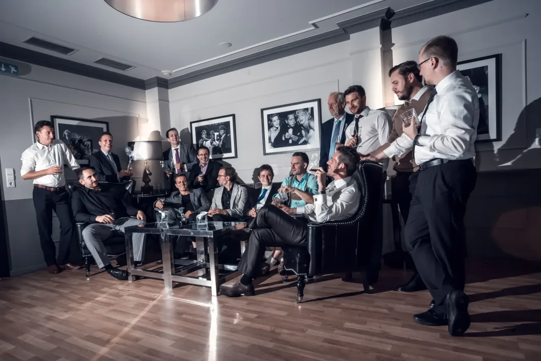 Männergruppe in Anzügen sitzt und steht in elegantem Raum, entspannte Unterhaltung.