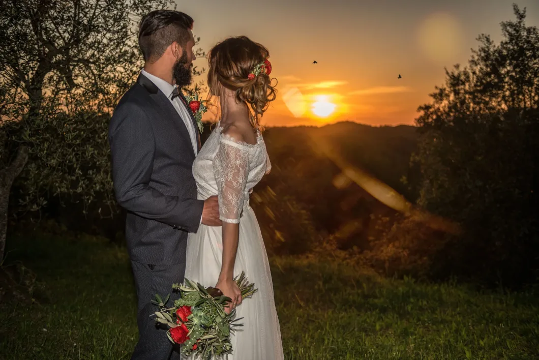 Brautpaar bei Sonnenuntergang, sie mit Blumenstrauß, romantische Kulisse.
