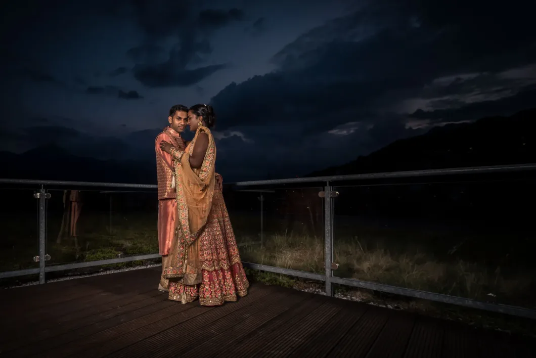 Hochzeitspaar bei Nacht auf Terrasse mit Bergen im Hintergrund, traditionell gekleidet.