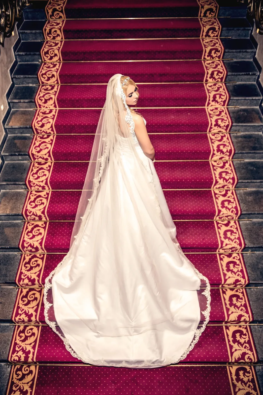 Braut in weißem Kleid mit Schleier auf prunkvoller Treppe.