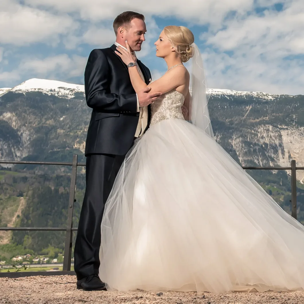 Brautpaar vor Berglandschaft, sie tragen elegantes Hochzeitskleid und Anzug.